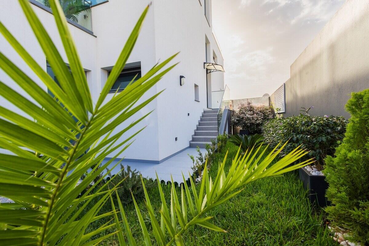A white modern house exterior features a staircase leading to an elevated entrance and garden — 16 Rua Encosta Dos Magos # B, FL