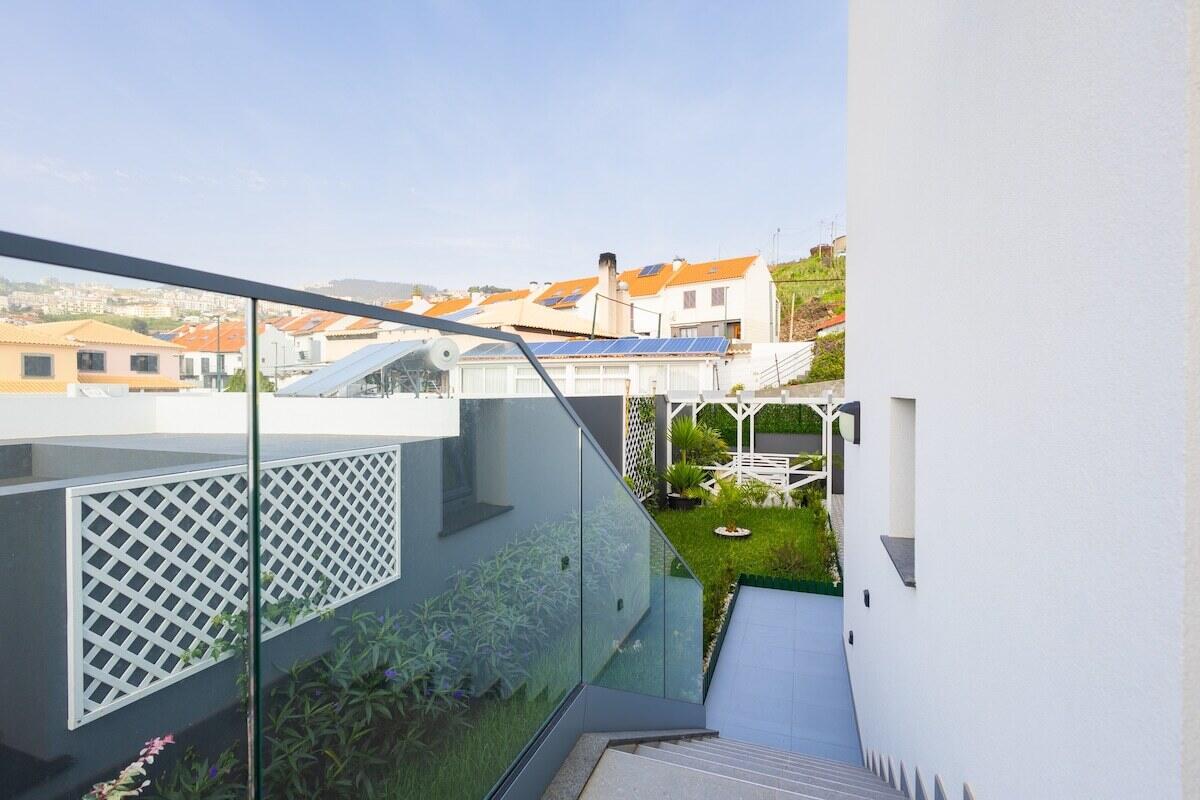 An outdoor staircase with a glass railing leads down to a small garden and patio — 16 Rua Encosta Dos Magos # B, FL