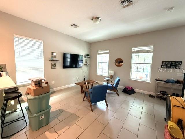 A living room features light-colored walls, tile flooring, two windows, and a wall-mounted television — 9362 WOODCRANE DRIVE, WINTER GARDEN, FL