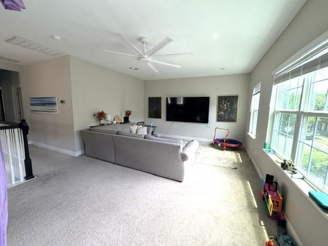 A spacious living room features a large gray sectional sofa, a wall-mounted television, and carpeted floors — 9362 WOODCRANE DRIVE, WINTER GARDEN, FL