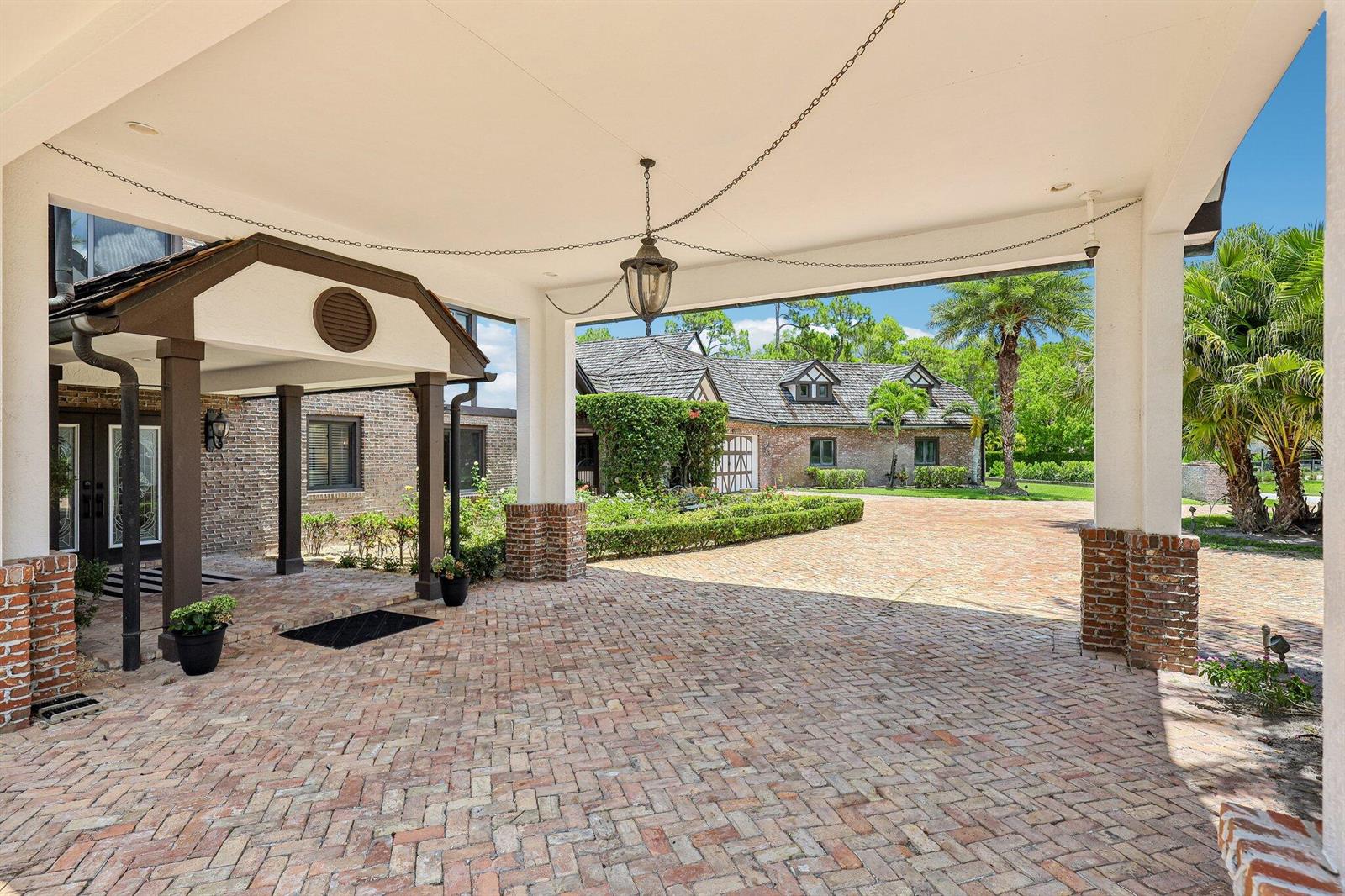 A brick-paved porte-cochère leads to a courtyard with a brick house and lush landscaping — 14900 Stirrup Lane, Wellington FL 33414, WELLINGTON, FL
