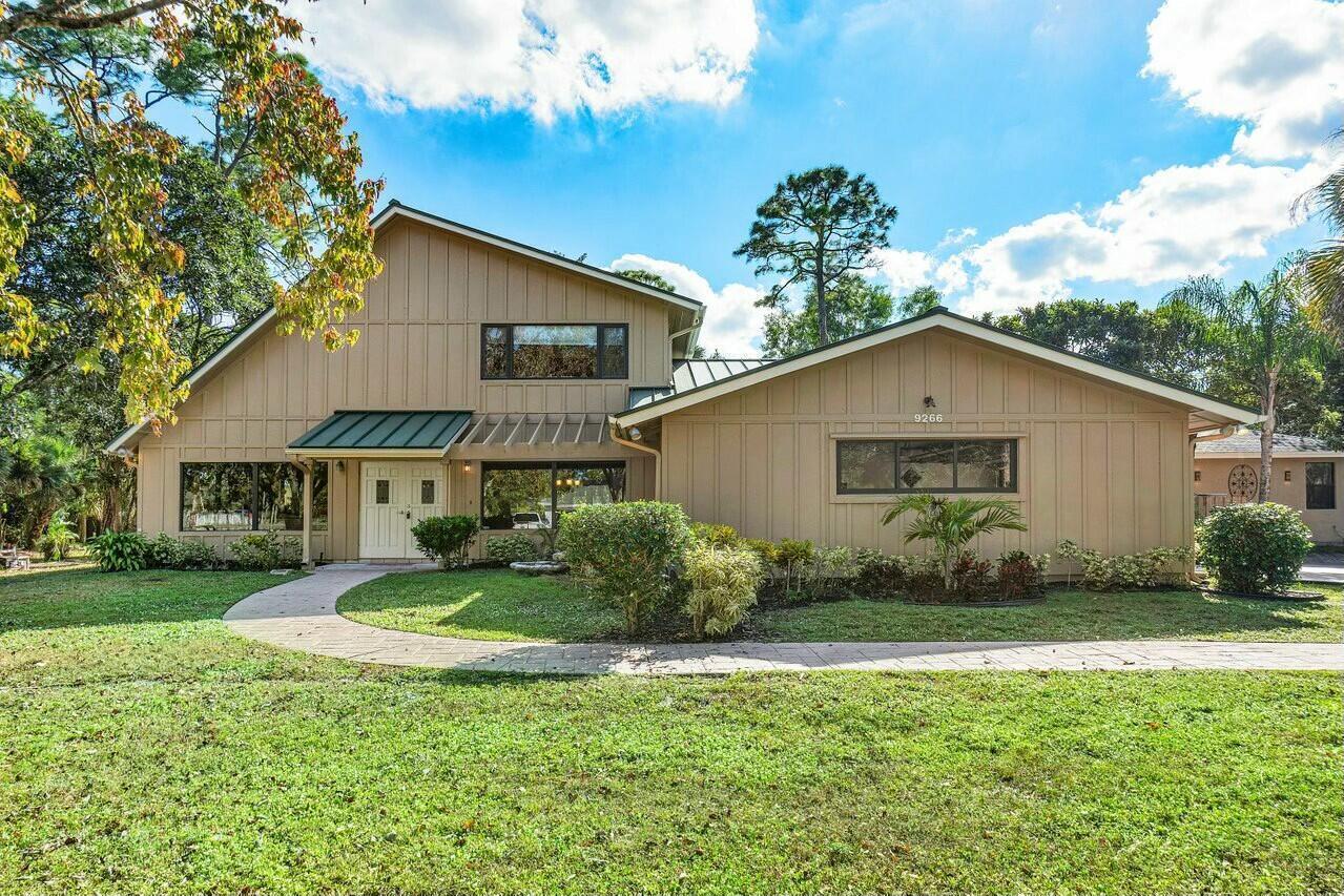 A two-story house with tan vertical siding, a green metal roof, and a curved walkway — 9266 Pinion Drive, Lake Worth FL 33467, LAKE WORTH, FL