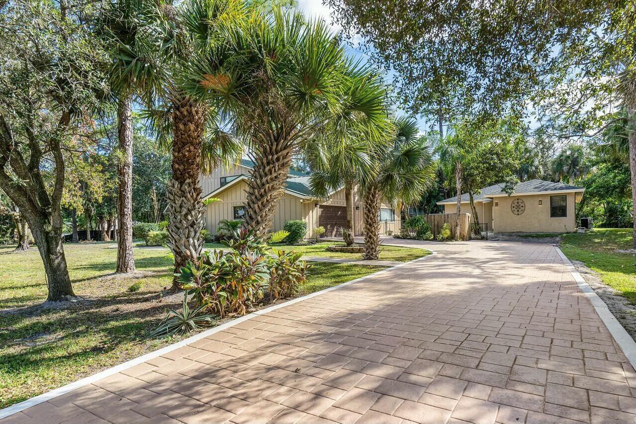 A paved driveway leads to a tan house with palm trees and a detached garage — 9266 Pinion Drive, Lake Worth FL 33467, LAKE WORTH, FL