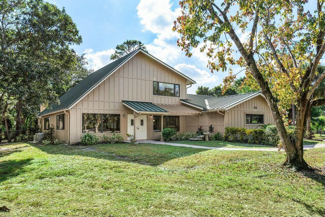 A two-story house with tan vertical siding and a green metal roof sits on grass — 9266 Pinion Drive, Lake Worth FL 33467, LAKE WORTH, FL