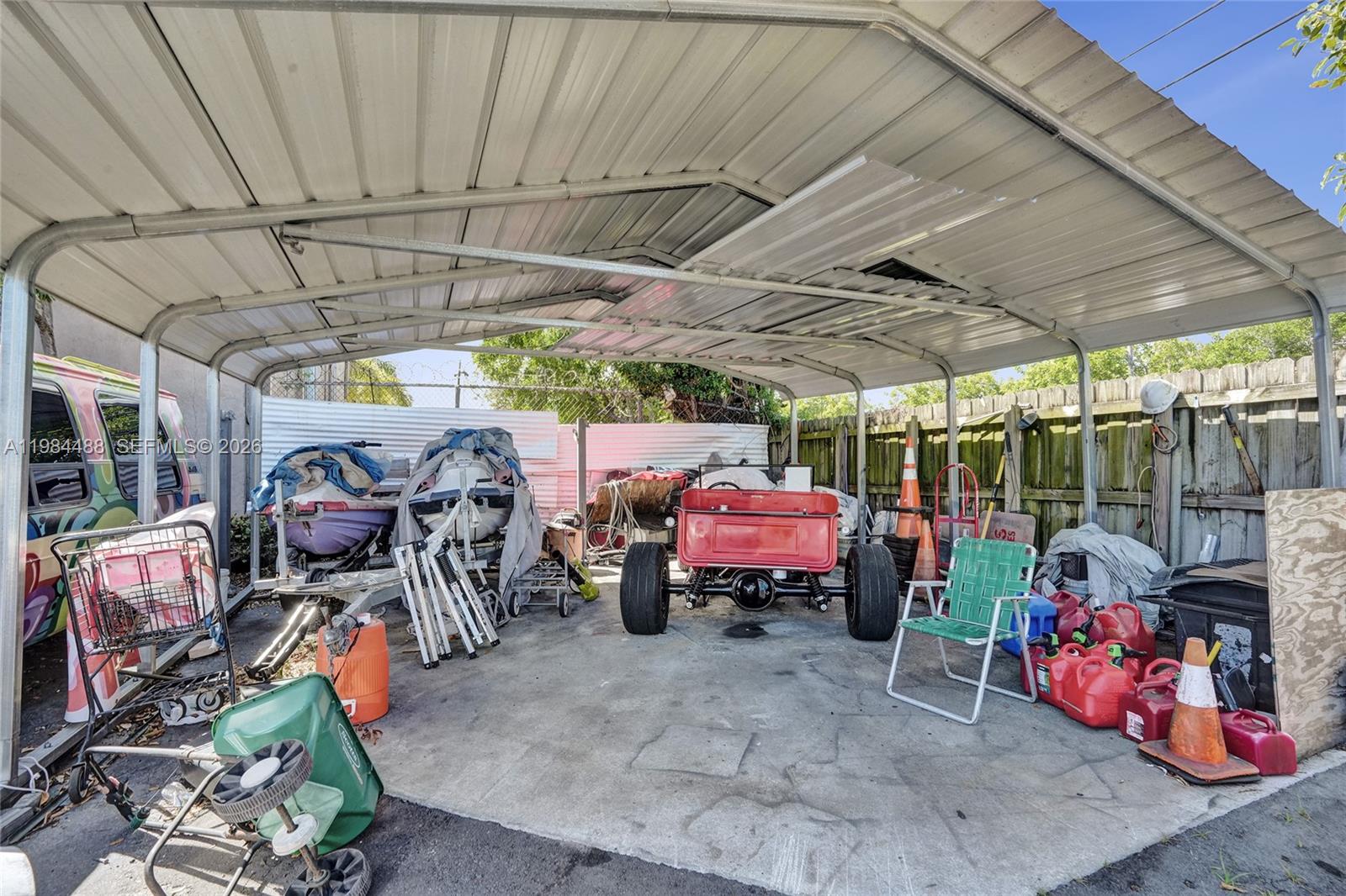 An outdoor metal carport contains a red vehicle frame, a boat, and various stored items — 345 COPANS RD, Pompano Beach FL 33064, POMPANO BEACH, FL