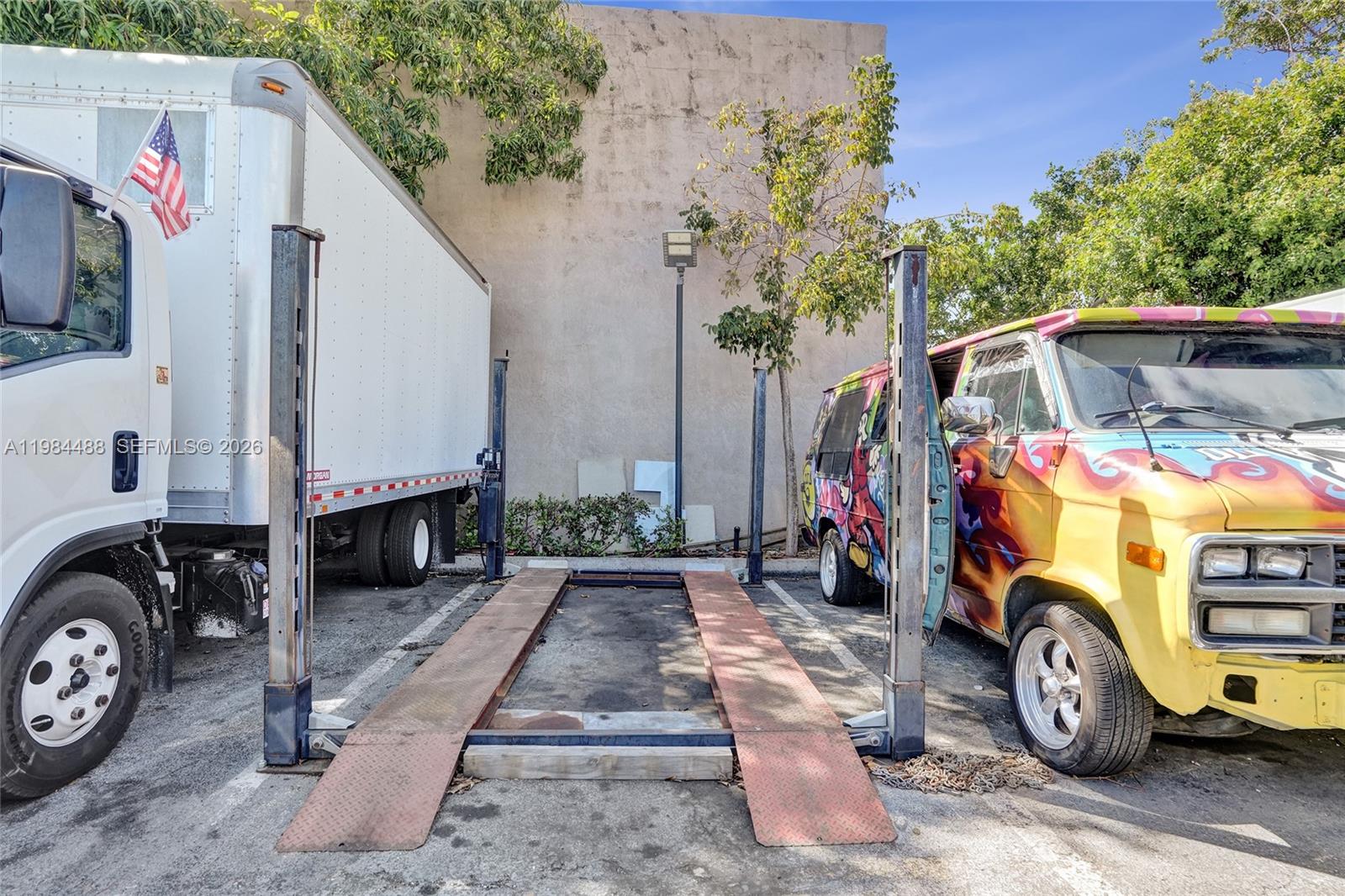 An outdoor vehicle lift is situated between a white box truck and a painted van — 345 COPANS RD, Pompano Beach FL 33064, POMPANO BEACH, FL