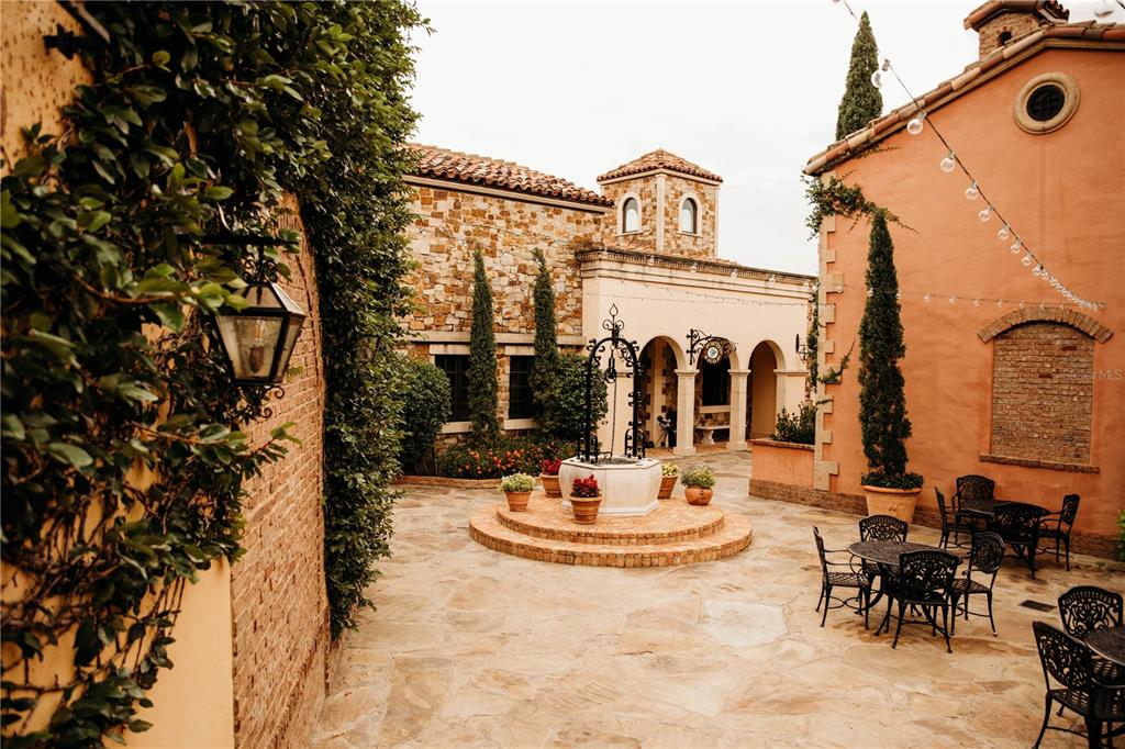 An outdoor stone courtyard features a central wishing well, patio furniture, and Mediterranean-style architecture — 15414 APENNINE WAY, MONTVERDE, FL