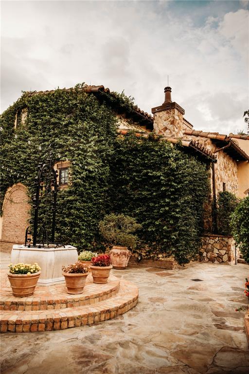 A stone house exterior features a climbing vine, a stone well, and potted flowers — 15414 APENNINE WAY, MONTVERDE, FL