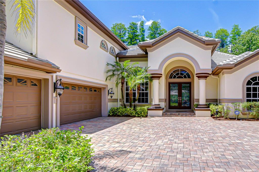 The exterior of a beige house features a paved driveway, a double garage, and an arched entryway — 20915 LAKE VIENNA DRIVE, LAND O LAKES, FL