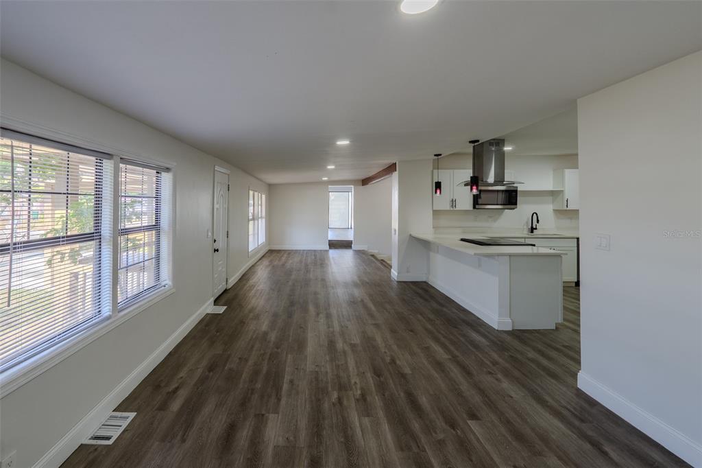 An open-concept living area features wood-look flooring, white walls, and a kitchen with white cabinetry — 599 CAROLINA AVENUE, FORT MYERS, FL