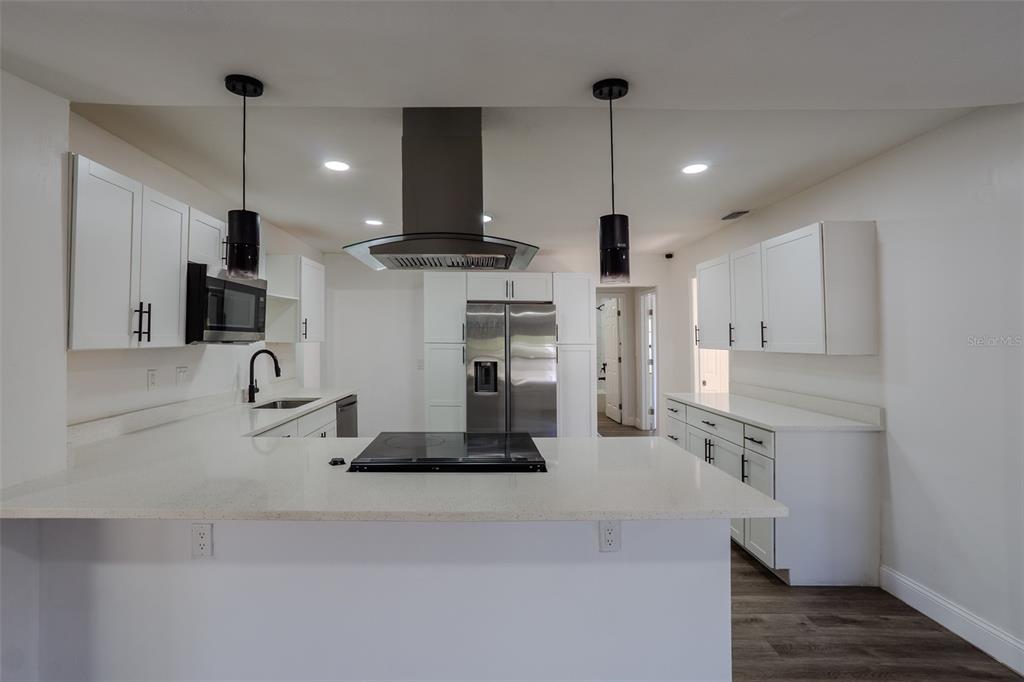 A modern kitchen features white cabinets, stainless steel appliances, a center island, and pendant lighting — 599 CAROLINA AVENUE, FORT MYERS, FL