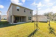 The rear exterior of a two-story beige house features a covered patio and grassy yard — 5277 ROYAL POINT AVENUE, KISSIMMEE, FL