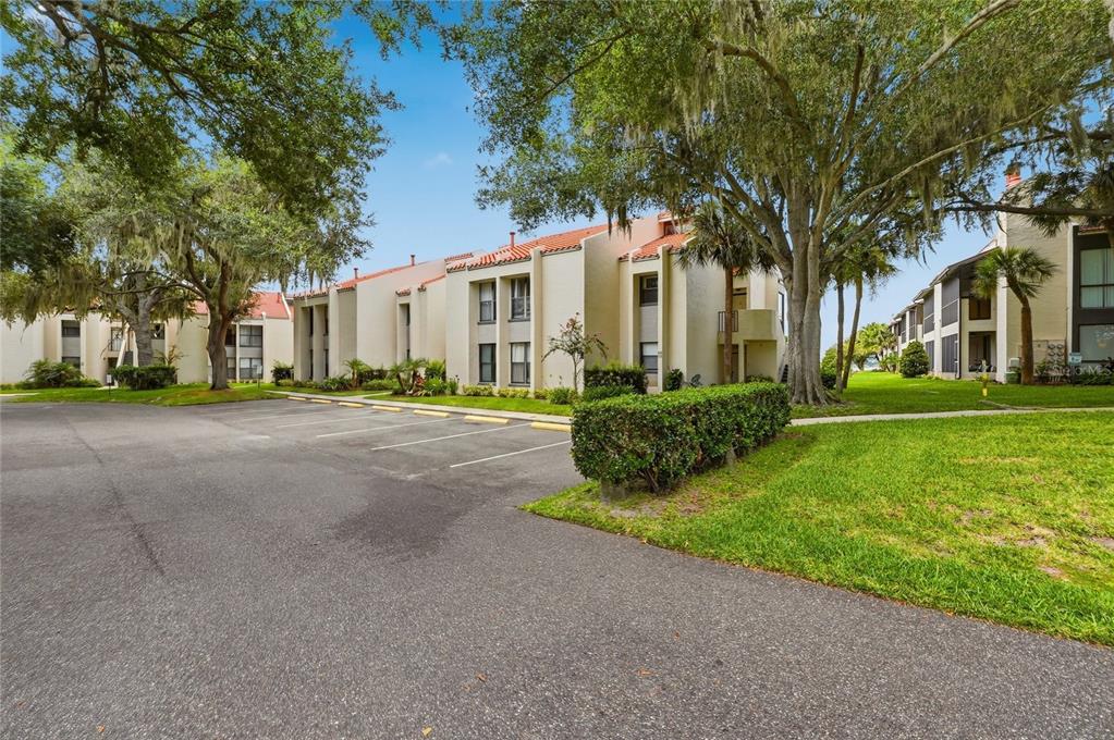 An exterior view of a multi-story apartment complex with a parking lot and mature trees — 503 SWEET BAY CIRCLE, WINTER HAVEN, FL