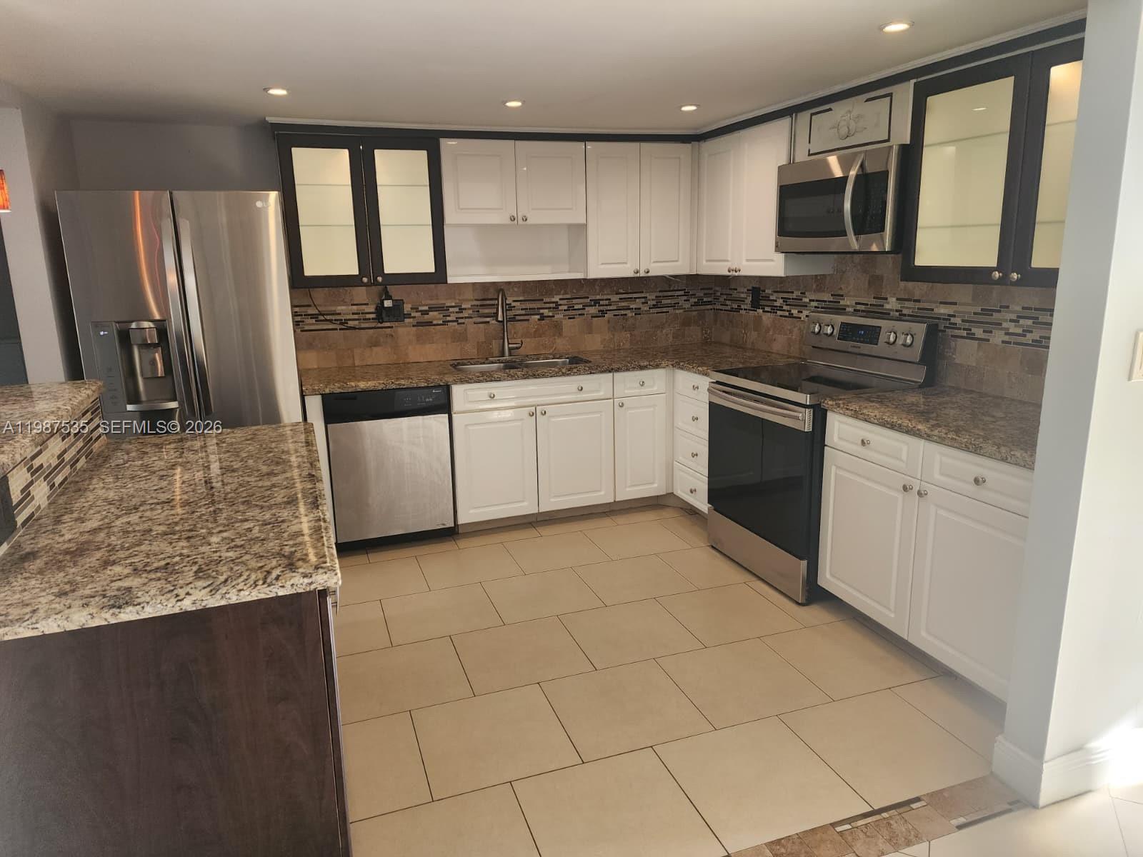 A kitchen features white cabinets, dark-framed glass upper cabinets, stainless steel appliances, and granite countertops — 537 N University Dr # 71, Plantation FL 33324, PLANTATION, FL