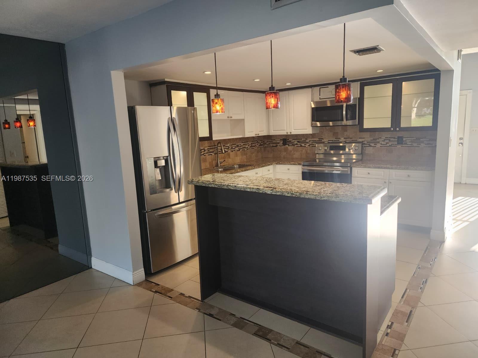 A kitchen features white and dark cabinetry, stainless steel appliances, and a granite-topped breakfast bar — 537 N University Dr # 71, Plantation FL 33324, PLANTATION, FL