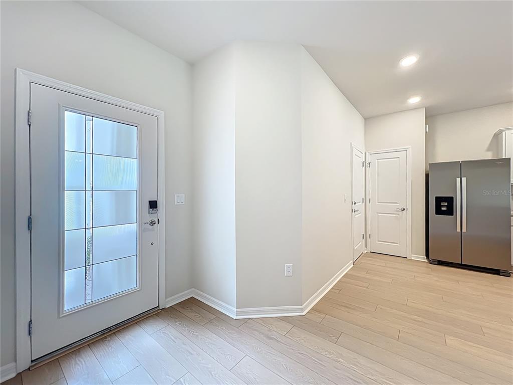 An entryway with light wood flooring, a white front door, and a stainless steel refrigerator — 431 MEADOWLAND POINT, OVIEDO, FL