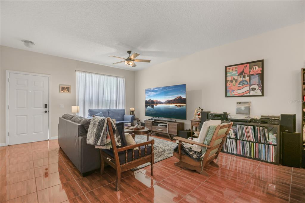 A living room features tile flooring, a ceiling fan, a television, and a vinyl collection — 3141 SUN LAKE COURT UNIT A, KISSIMMEE, FL