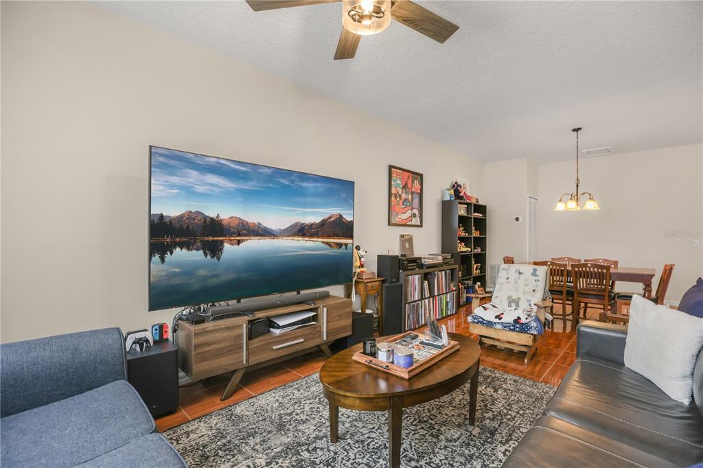 A living room with a large television, wood media console, coffee table, and dining area — 3141 SUN LAKE COURT UNIT A, KISSIMMEE, FL