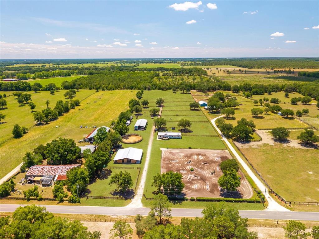 An aerial view shows a rural property with multiple barns, a riding arena, and pastures — 18350 SE 42ND PLACE, MORRISTON, FL