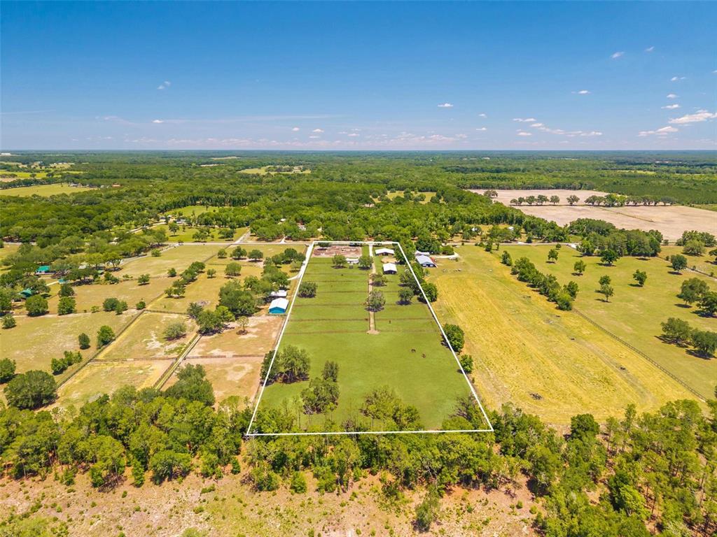 An aerial view shows a fenced rectangular pasture with outbuildings surrounded by rural wooded land — 18350 SE 42ND PLACE, MORRISTON, FL