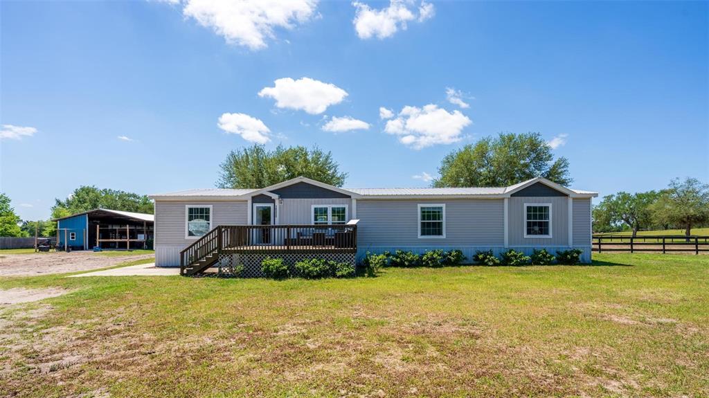 A single-story manufactured home with light gray siding and a wooden deck sits outdoors — 18350 SE 42ND PLACE, MORRISTON, FL