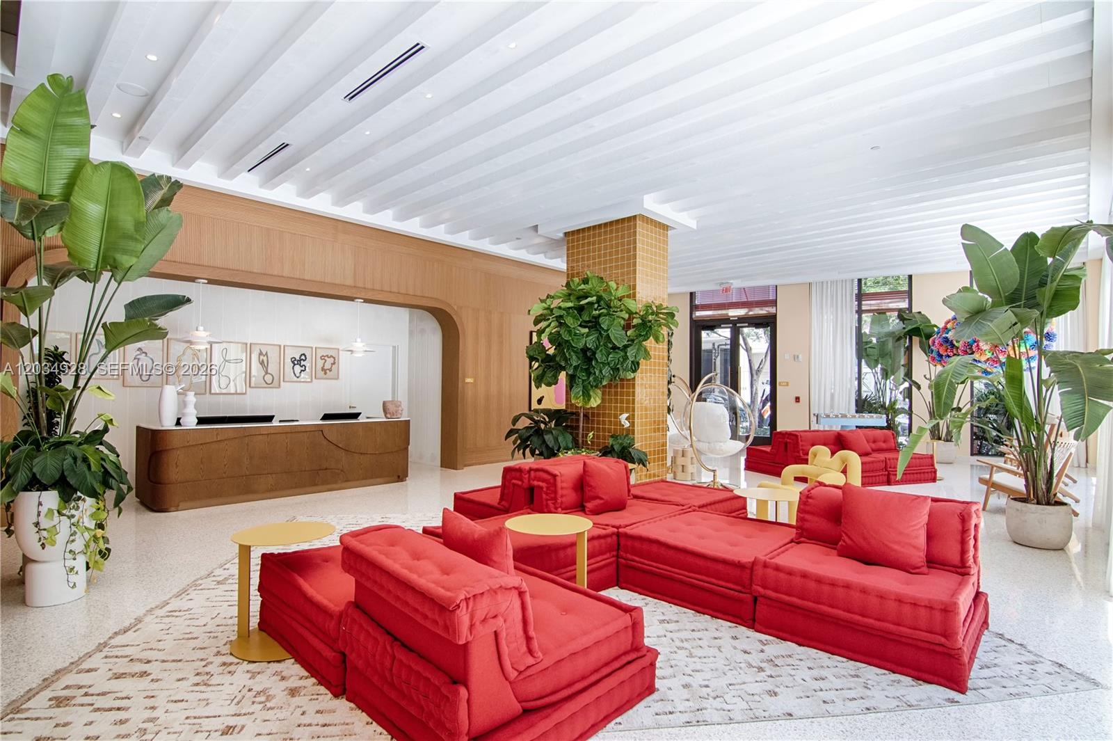 A hotel lobby features a reception desk, red modular seating, and large potted plants — 90 NE 32 # 520, Miami FL 33127, MIAMI, FL