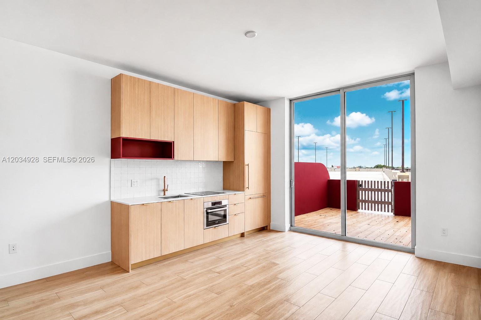 A modern kitchen with light wood cabinets, a red accent shelf, and a balcony entrance — 90 NE 32 # 520, Miami FL 33127, MIAMI, FL
