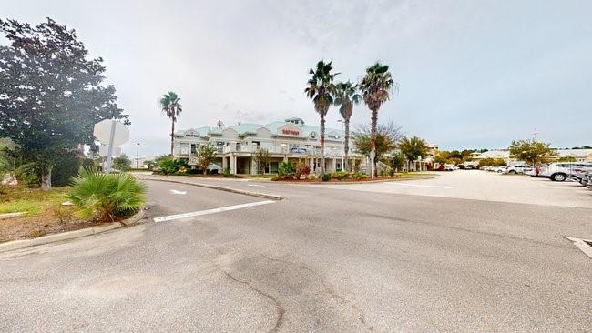 A low-rise commercial building with palm trees sits behind a large paved parking lot — 160 CYPRESS POINT PARKWAY UNIT A102, PALM COAST, FL