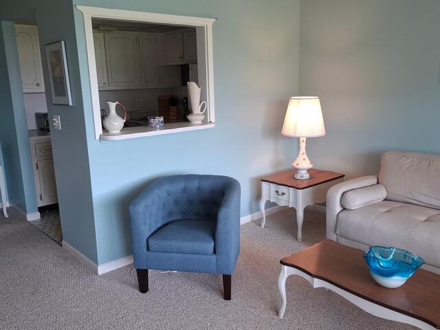 A living room features a blue armchair, a sofa, a side table with a lamp, and a pass-through window — 620 Horizon W # 202, Boynton Beach FL 33435, BOYNTON BEACH, FL