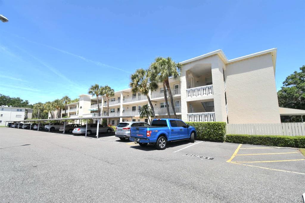 A multi-story apartment building with covered parking and a blue pickup truck in the foreground — 936 VIRGINIA STREET UNIT 206, DUNEDIN, FL