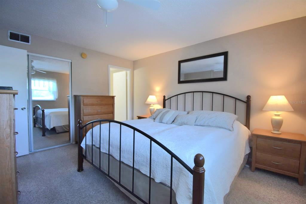 A bedroom features a metal-framed bed, two nightstands with lamps, and a mirrored closet — 936 VIRGINIA STREET UNIT 206, DUNEDIN, FL