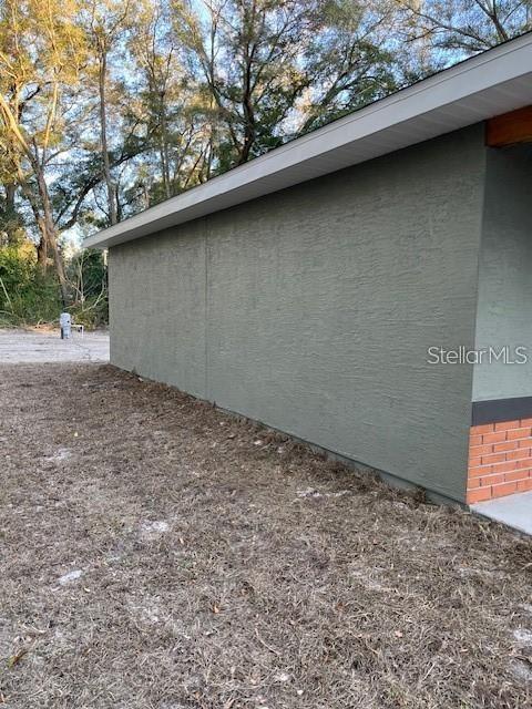 A side view of a house exterior featuring green stucco walls and a brick base — 3779 SE 140TH LANE, SUMMERFIELD, FL
