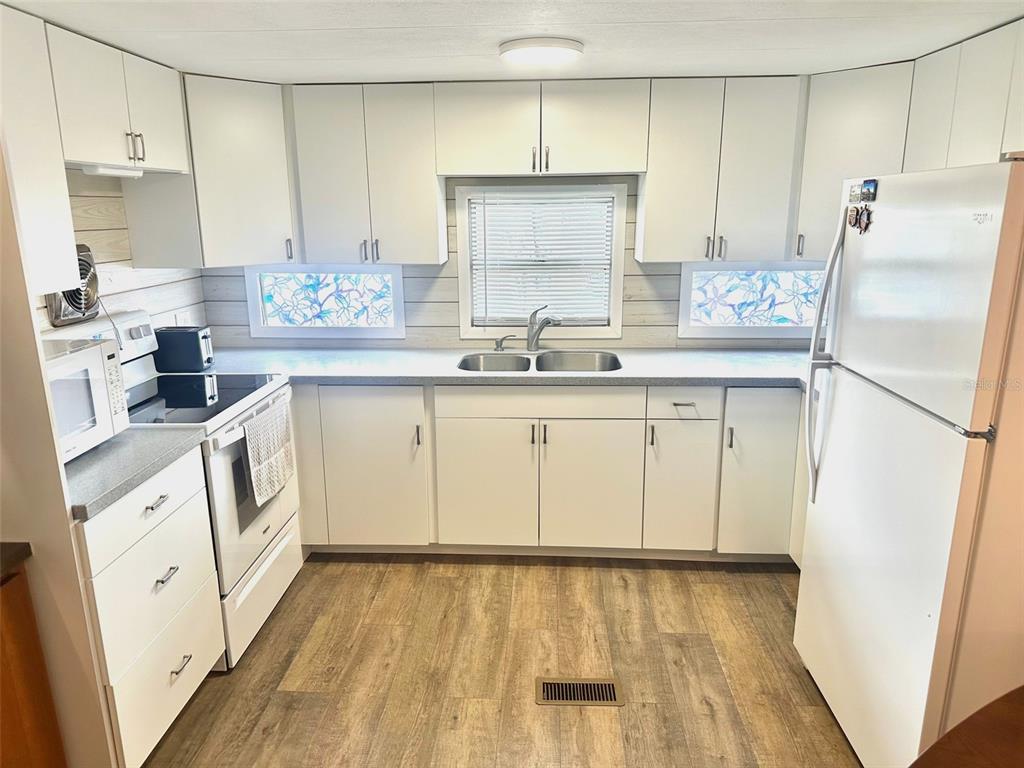 A kitchen features white cabinets, a white stove, a refrigerator, and wood-look flooring — 9790 66TH STREET N UNIT 362, PINELLAS PARK, FL