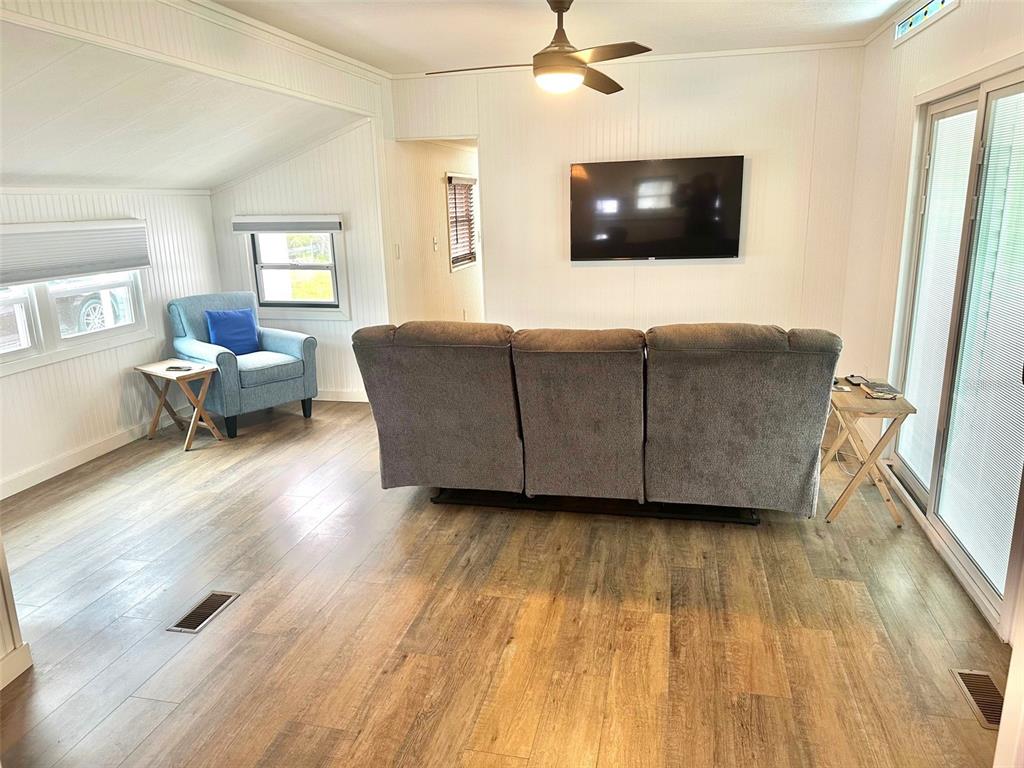 A living room features wood-look flooring, a gray reclining sofa, a blue armchair, and television — 9790 66TH STREET N UNIT 362, PINELLAS PARK, FL