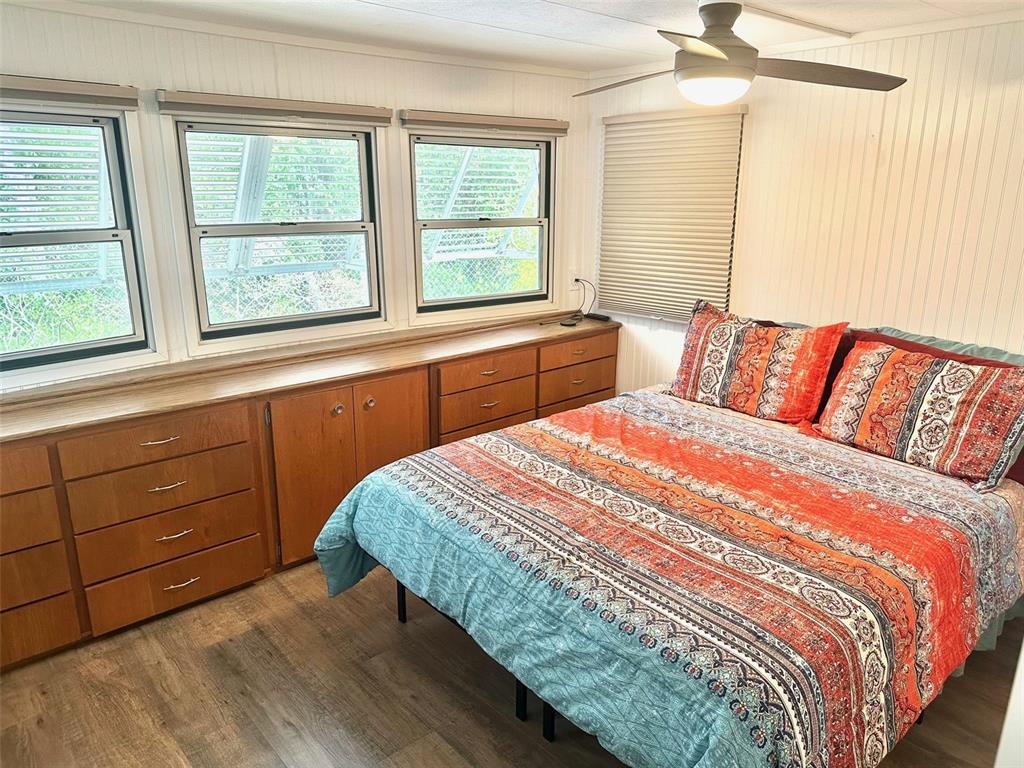 A bedroom features wood-look flooring, a built-in dresser, three windows, and a patterned bedspread — 9790 66TH STREET N UNIT 362, PINELLAS PARK, FL