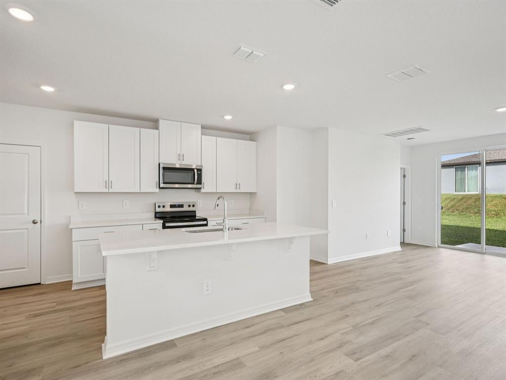 A modern kitchen with white cabinets, a central island, and light wood-look flooring — 3764 MOSCATO DRIVES, BROOKSVILLE, FL
