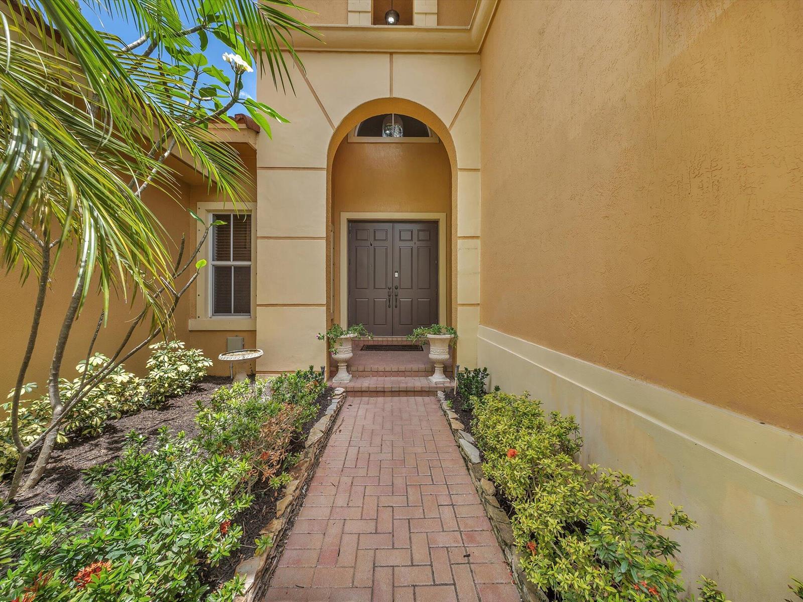 A brick walkway leads to the arched entryway of a house with tan stucco walls — 7678 NW 117th Lane, Parkland FL 33076, PARKLAND, FL