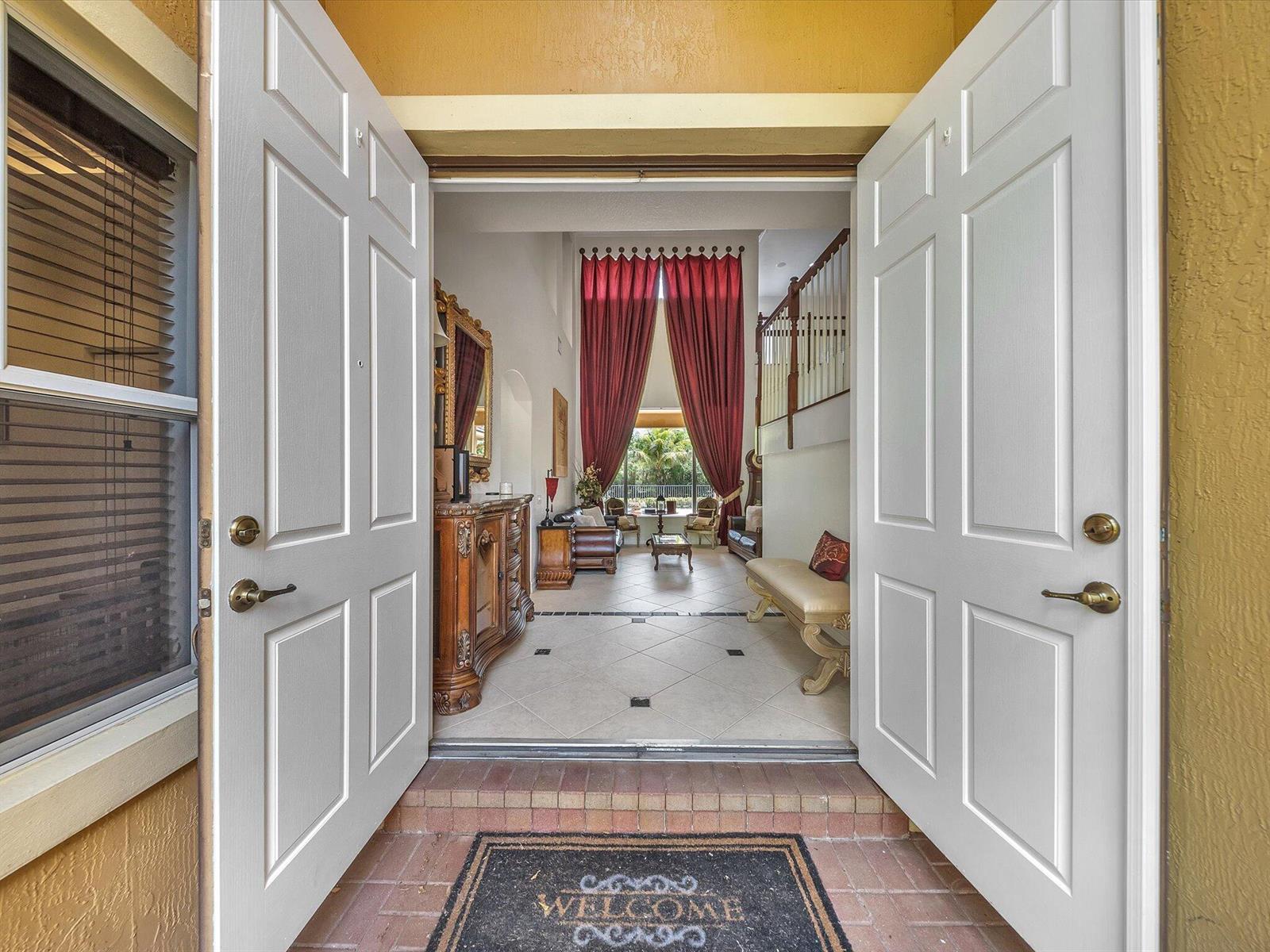 A view through open double doors into a foyer with tile floors and red curtains — 7678 NW 117th Lane, Parkland FL 33076, PARKLAND, FL