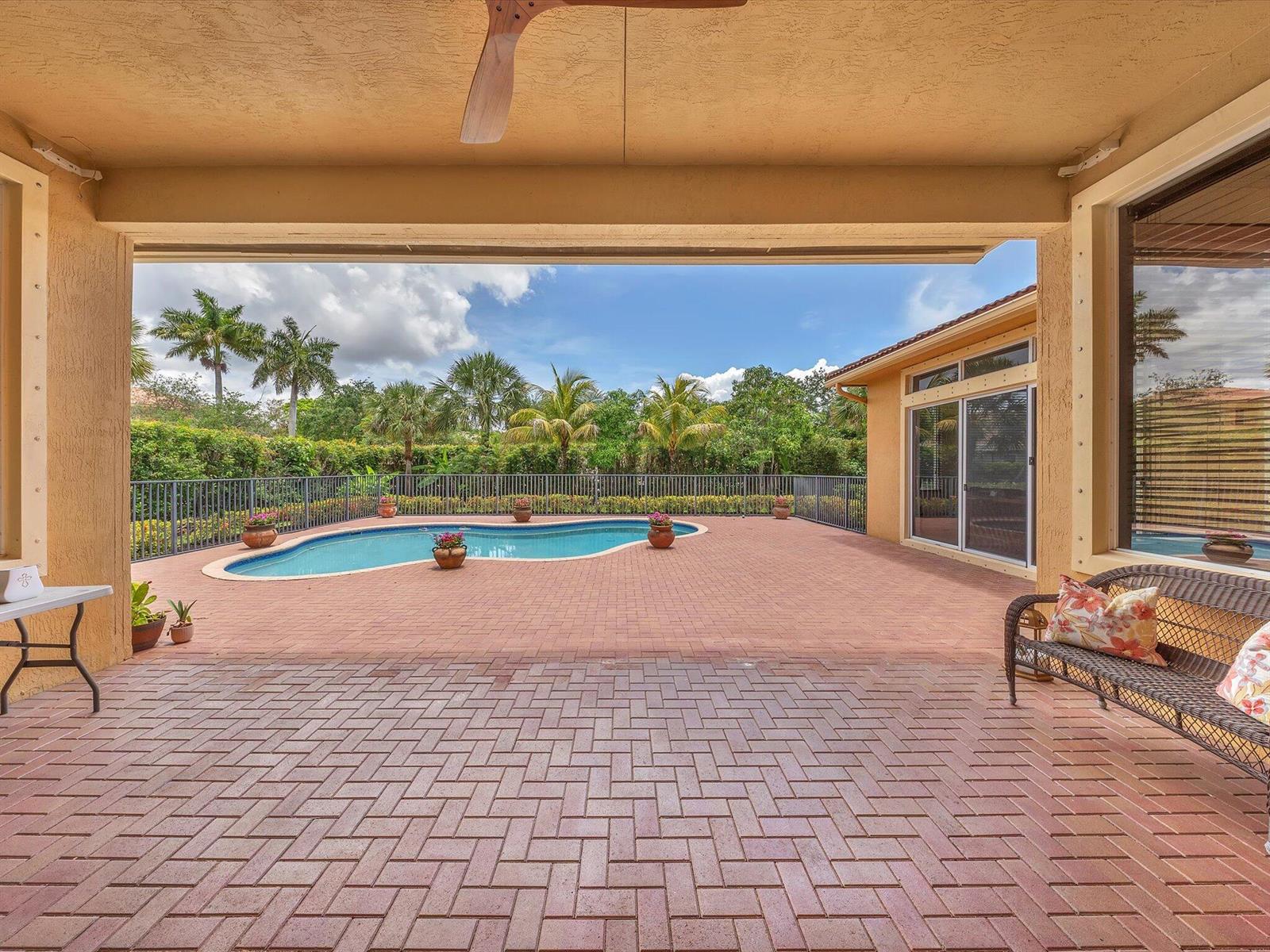 A covered patio features brick pavers, a swimming pool, and a view of palm trees — 7678 NW 117th Lane, Parkland FL 33076, PARKLAND, FL