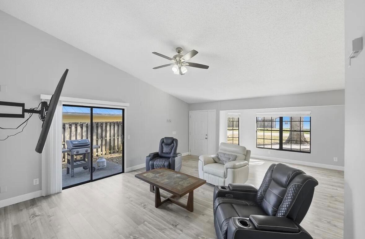 A living room with light wood-look flooring, a ceiling fan, and sliding glass patio doors — 2890 1st Place, Vero Beach FL 32968, VERO BEACH, FL