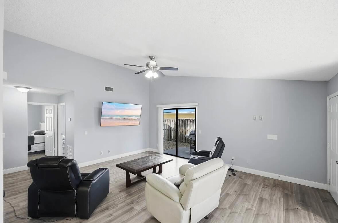 A living room with light gray walls, wood-look flooring, a ceiling fan, and sliding glass doors — 2890 1st Place, Vero Beach FL 32968, VERO BEACH, FL