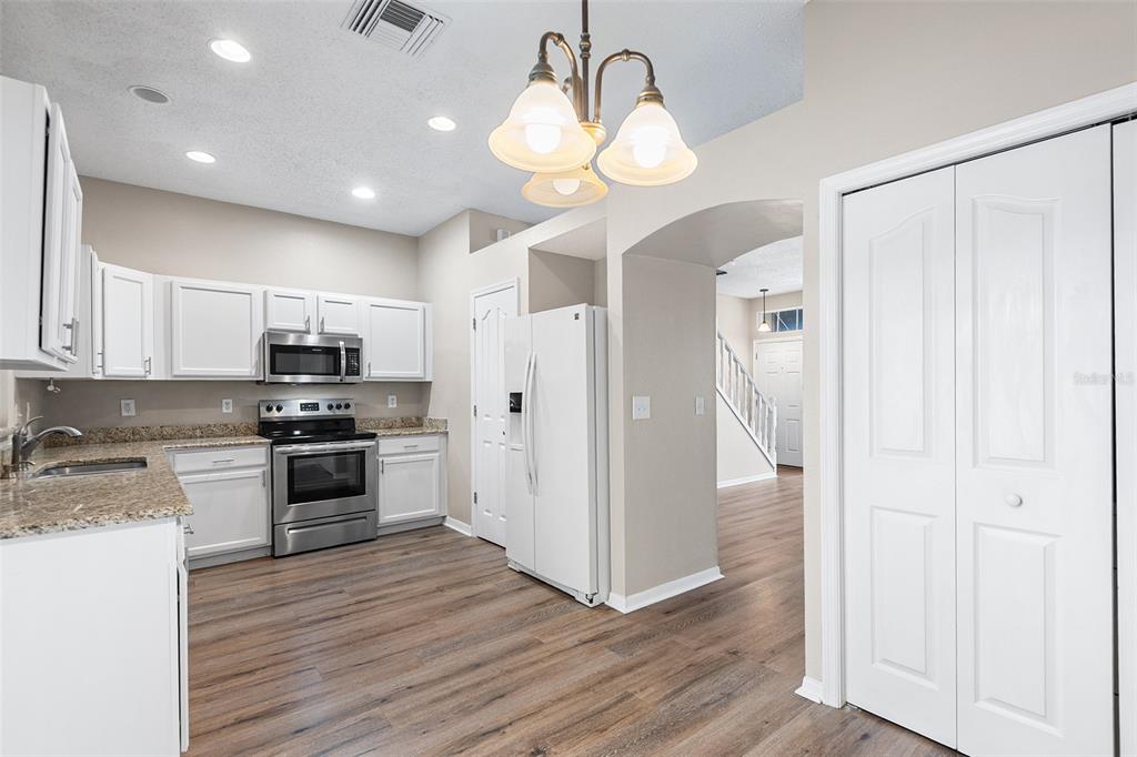 A kitchen with white cabinets, stainless steel appliances, granite countertops, and wood-look flooring — 10114 FARMINGDALE PLACE, TAMPA, FL