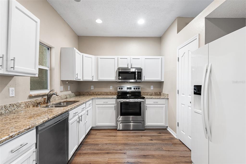 A kitchen features white cabinets, granite countertops, stainless steel appliances, and wood-look flooring — 10114 FARMINGDALE PLACE, TAMPA, FL