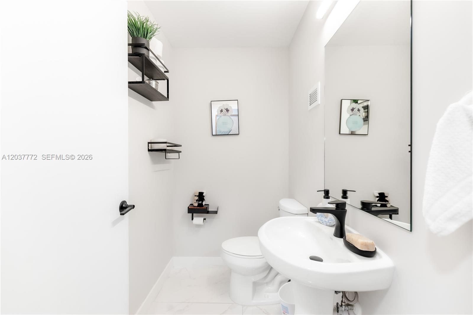 A modern half bathroom features a pedestal sink, a wall-mounted mirror, and black shelving — 25657 SW 144th Ave, Homestead FL 33032, HOMESTEAD, FL