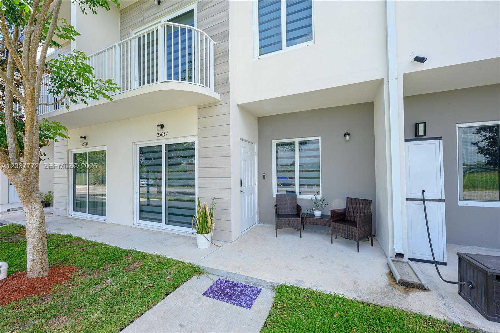 A two-story townhouse exterior features a concrete patio, sliding glass doors, and a balcony — 25657 SW 144th Ave, Homestead FL 33032, HOMESTEAD, FL