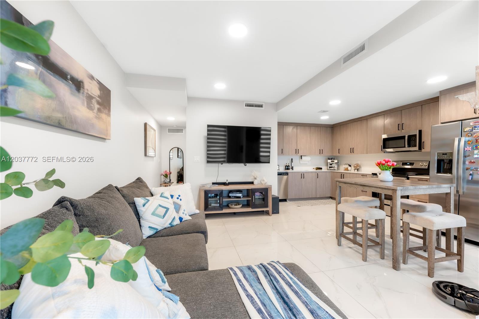 This open-concept living room and kitchen features light tile flooring and wood-toned cabinetry — 25657 SW 144th Ave, Homestead FL 33032, HOMESTEAD, FL