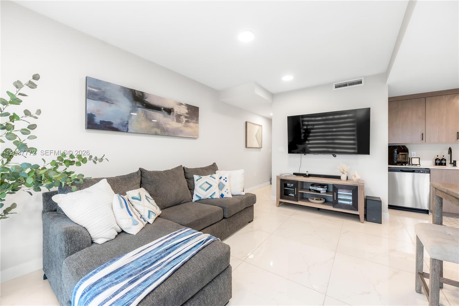 A living room features a grey sectional sofa, a wall-mounted television, and light-colored tile flooring — 25657 SW 144th Ave, Homestead FL 33032, HOMESTEAD, FL