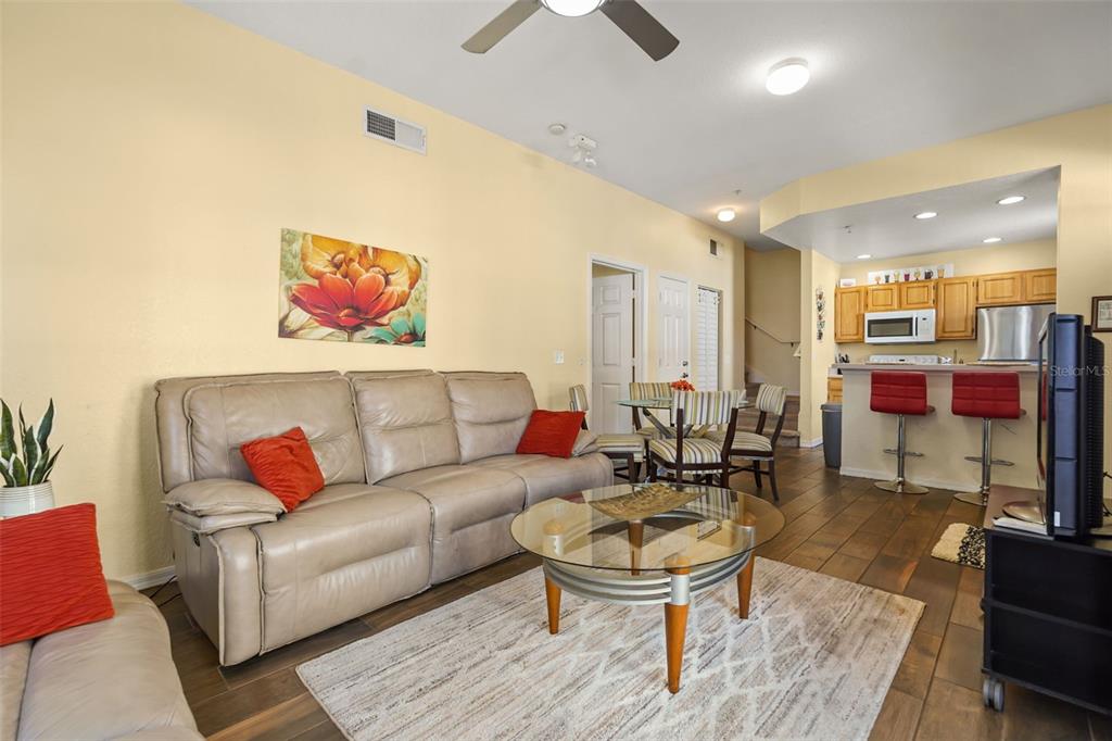 A living room with a beige sofa, glass coffee table, and an adjacent open kitchen — 4021 VENETIAN BAY DRIVE UNIT 101, KISSIMMEE, FL