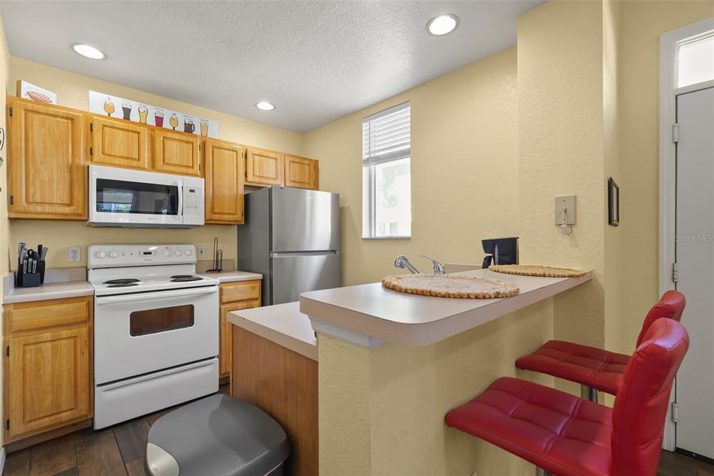 A kitchen features light wood cabinets, white appliances, a stainless refrigerator, and a breakfast bar — 4021 VENETIAN BAY DRIVE UNIT 101, KISSIMMEE, FL