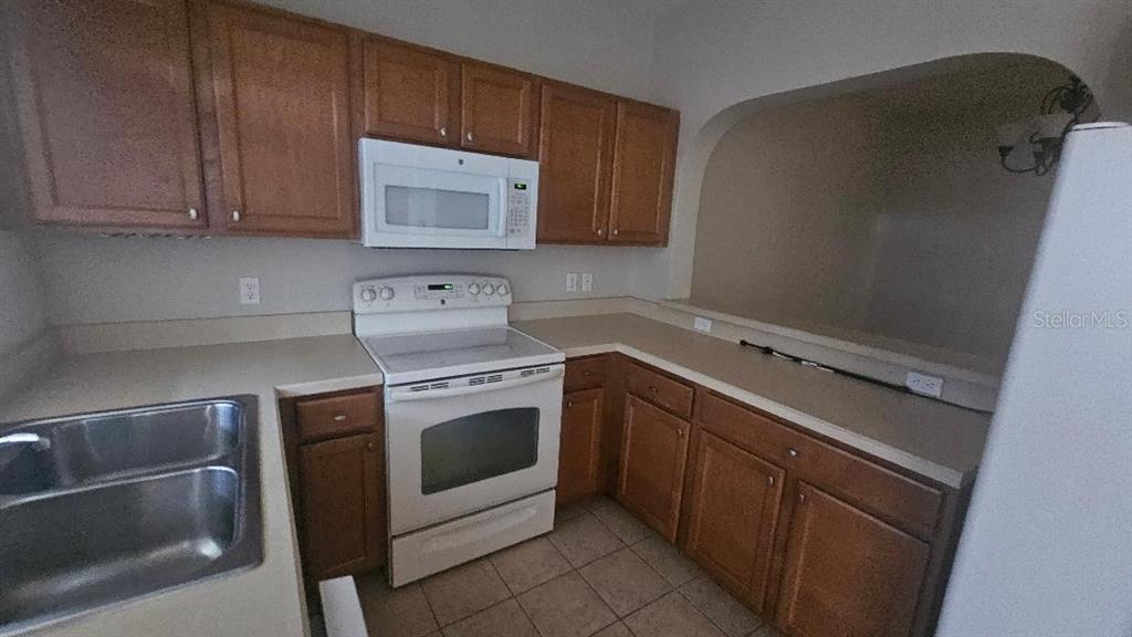 A kitchen features wood cabinets, white appliances, and a beige countertop with a double sink — 3909 45TH TERRACE W UNIT 106, BRADENTON, FL